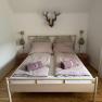 Bedroom with double bed, pink bed linen and towels, wooden floor and wall decoration.