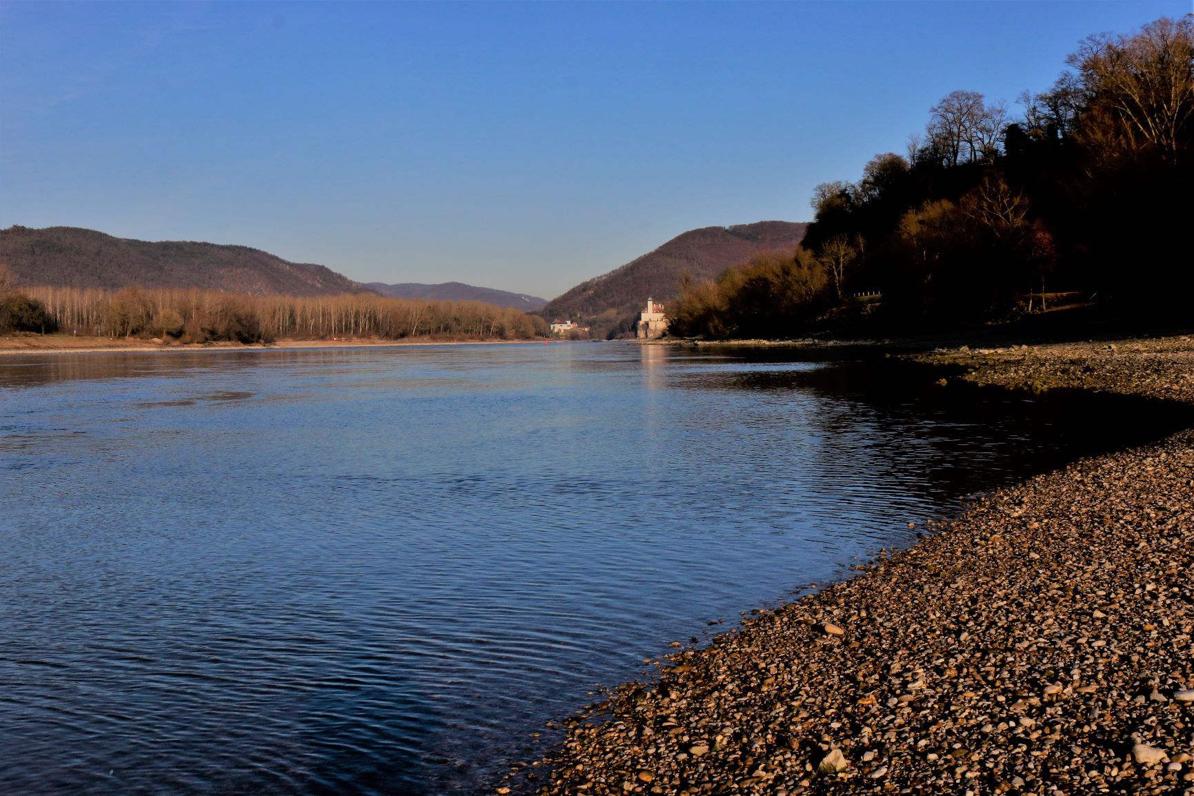 Riverbank with pebble beach and wooded hills in the background.