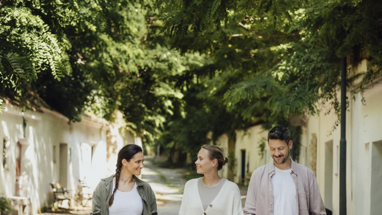 Three people are walking along a tree-lined path in Poysdorf.