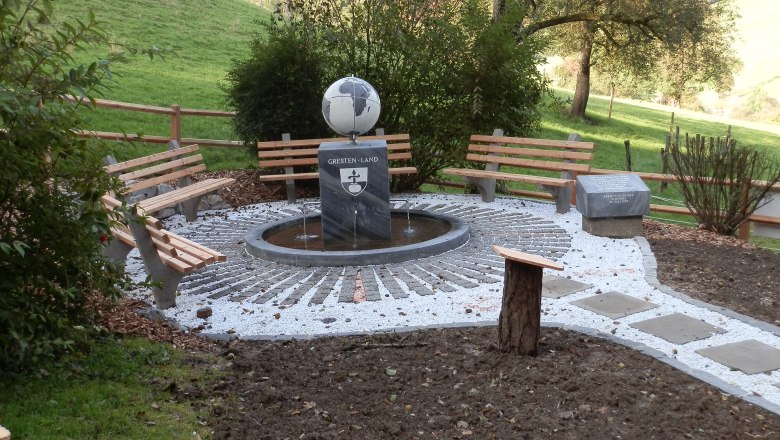 A rest area with benches and a meridian stone in a rural setting.