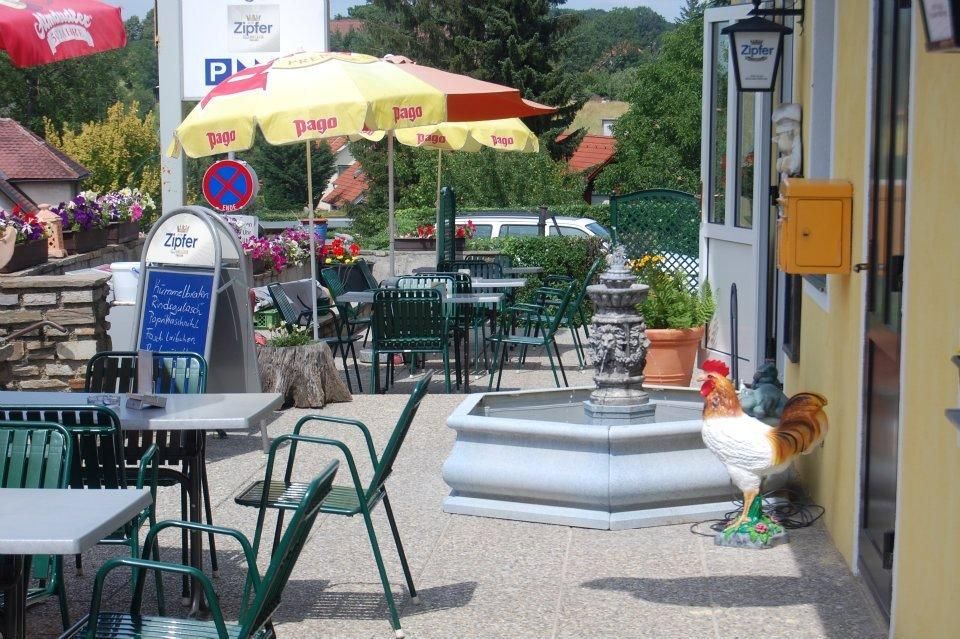 A guest garden with tables, chairs, parasols and a fountain. A rooster stands next to the fountain.