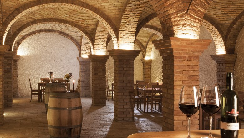 Wine cellar with brick arches, tables and wine barrels, illuminated by candles and lamps.