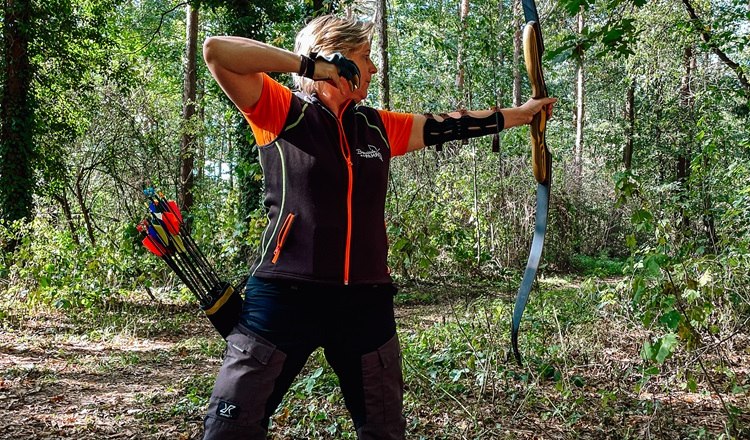 Person archery in the forest with bow and arrow.