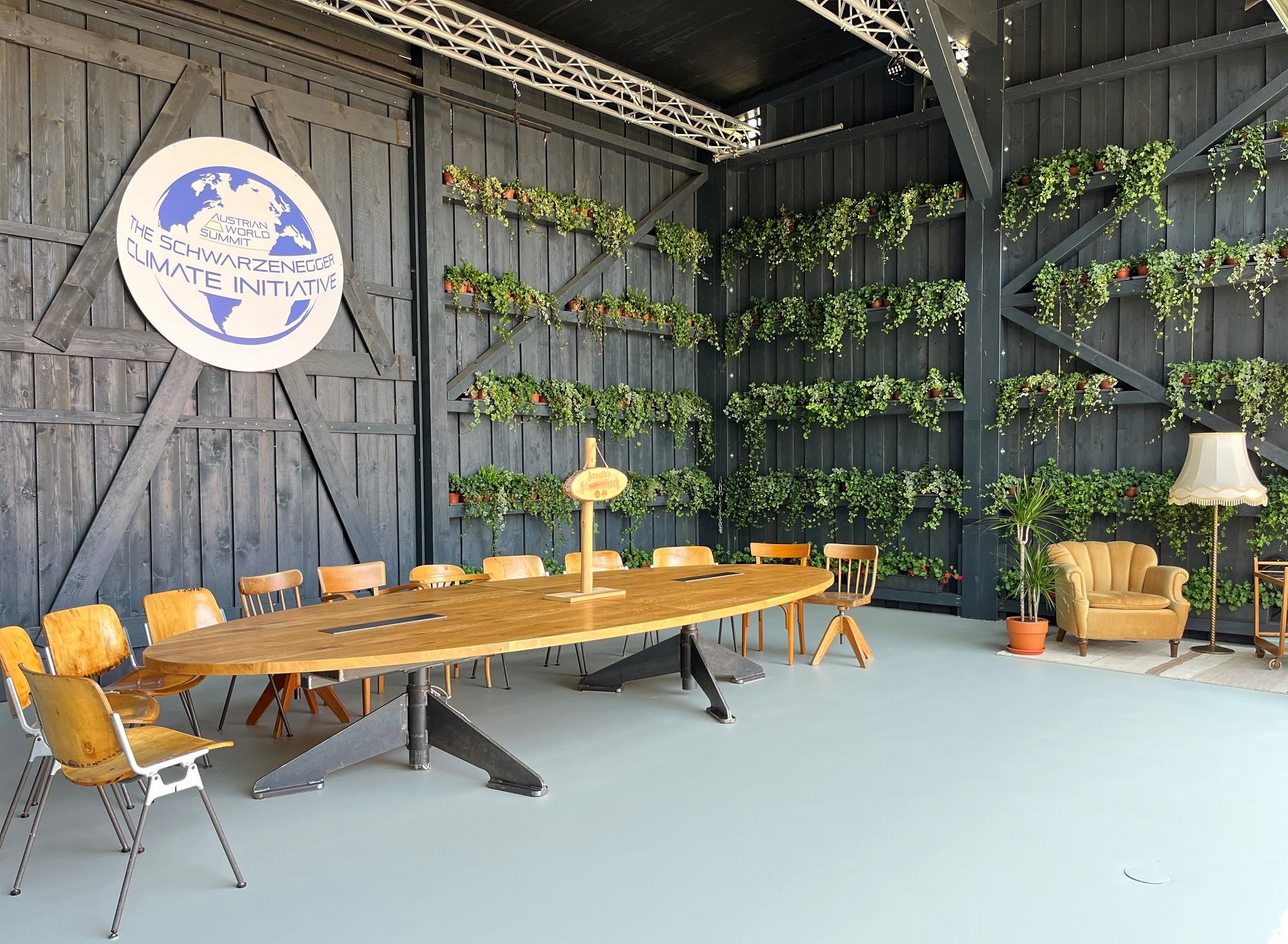 A modern meeting room with a wooden table, chairs and plants on the walls. A logo of the Schwarzenegger Climate Initiative is visible.