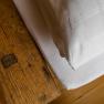 Close-up of a rustic wooden table next to a bed with white bed linen.