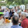 People sit at outdoor tables under vines and chat.