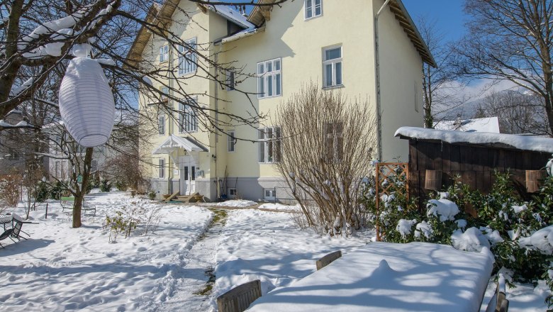 Snow-covered garden with table and chairs in front of a yellow house.