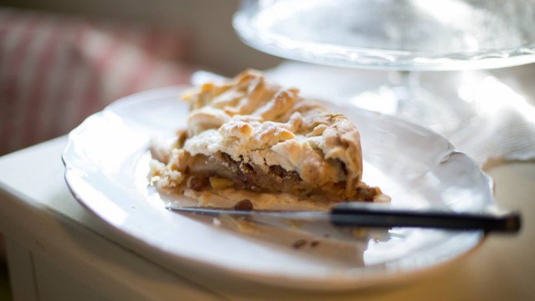 A piece of apple pie on a white plate with a knife next to it.