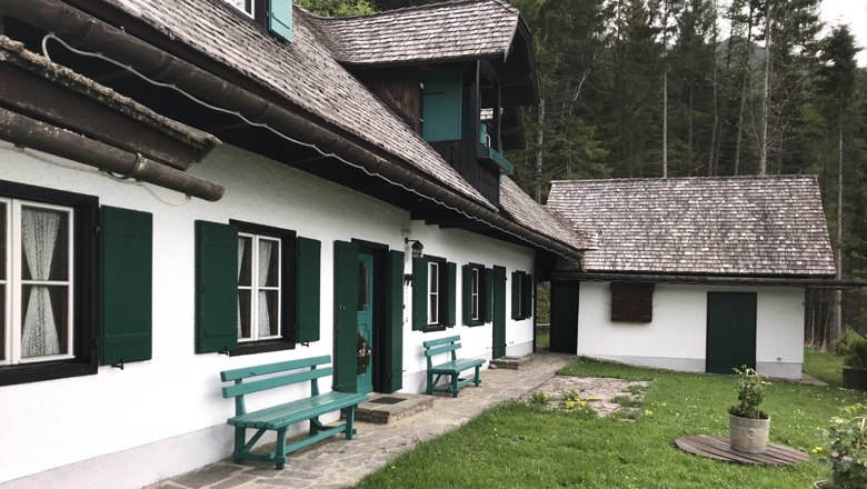 A traditional vacation home with green shutters and wooden benches in front of a forest.
