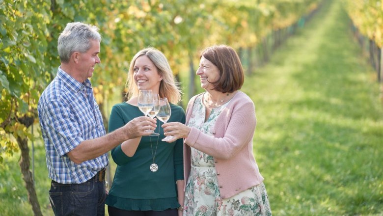 Three people clink glasses in a vineyard.