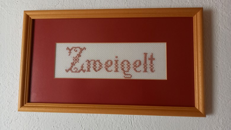 Embroidered picture with the word 'Zweigelt' in a wooden frame.