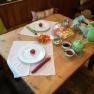 A laid breakfast table with plates, cutlery, cold cuts, vegetables and drinks.