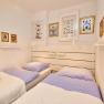 Two single beds with blue striped bed linen in a bright bedroom with decorative pictures on the wall.