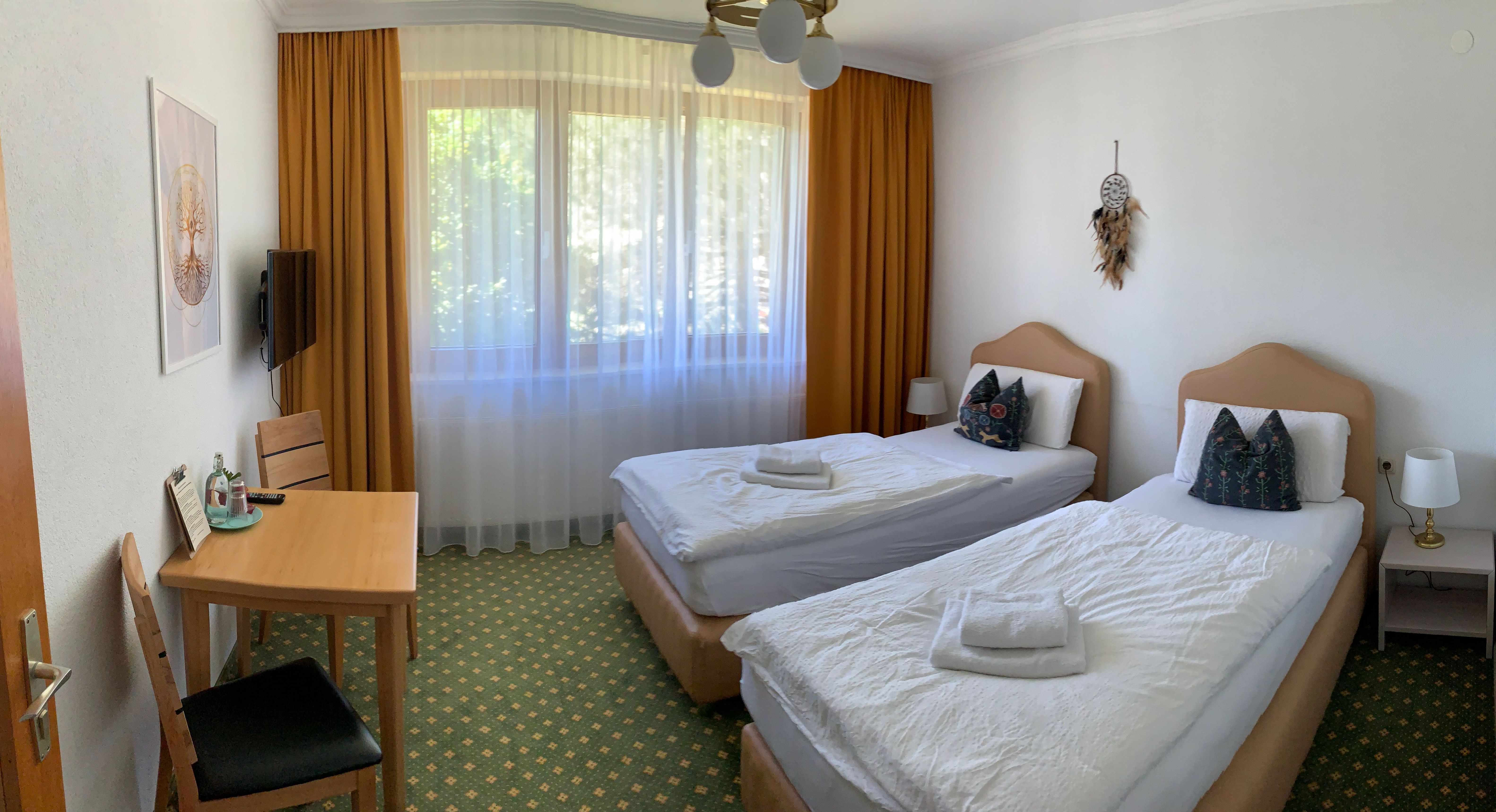 A hotel room with two single beds, a table with chairs and a window with curtains.