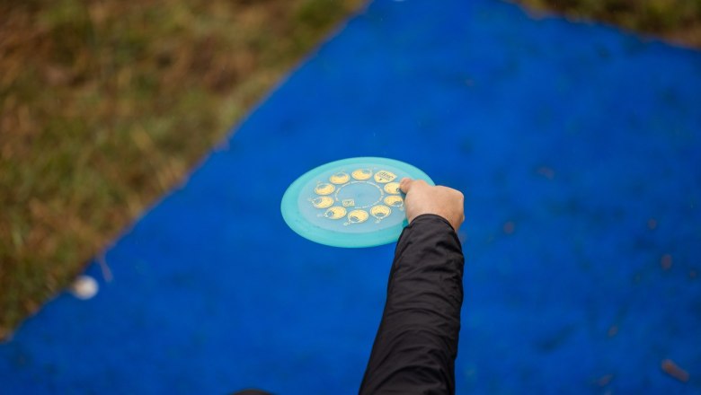Person holds a disc golf target over a blue mat, hand outstretched for the throw