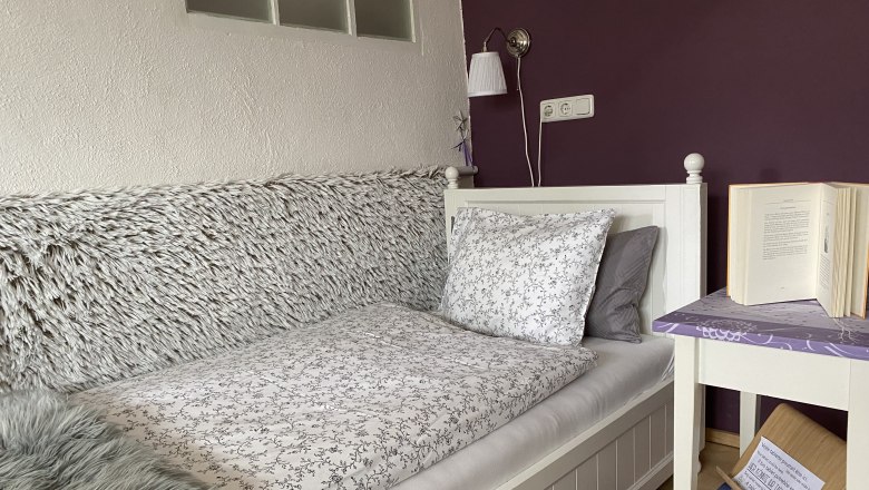 Cozy bedroom with single bed, purple wall, bedside table with book and lamp.