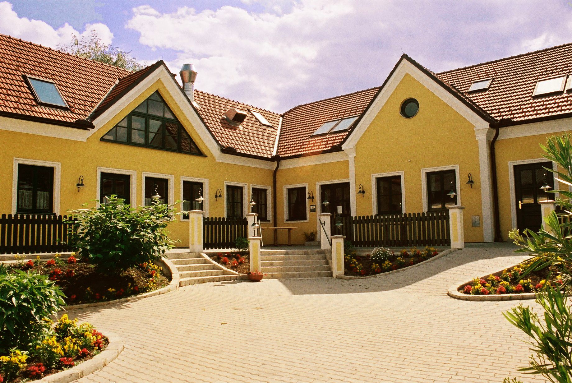 Yellow building with red tiled roofs and garden.