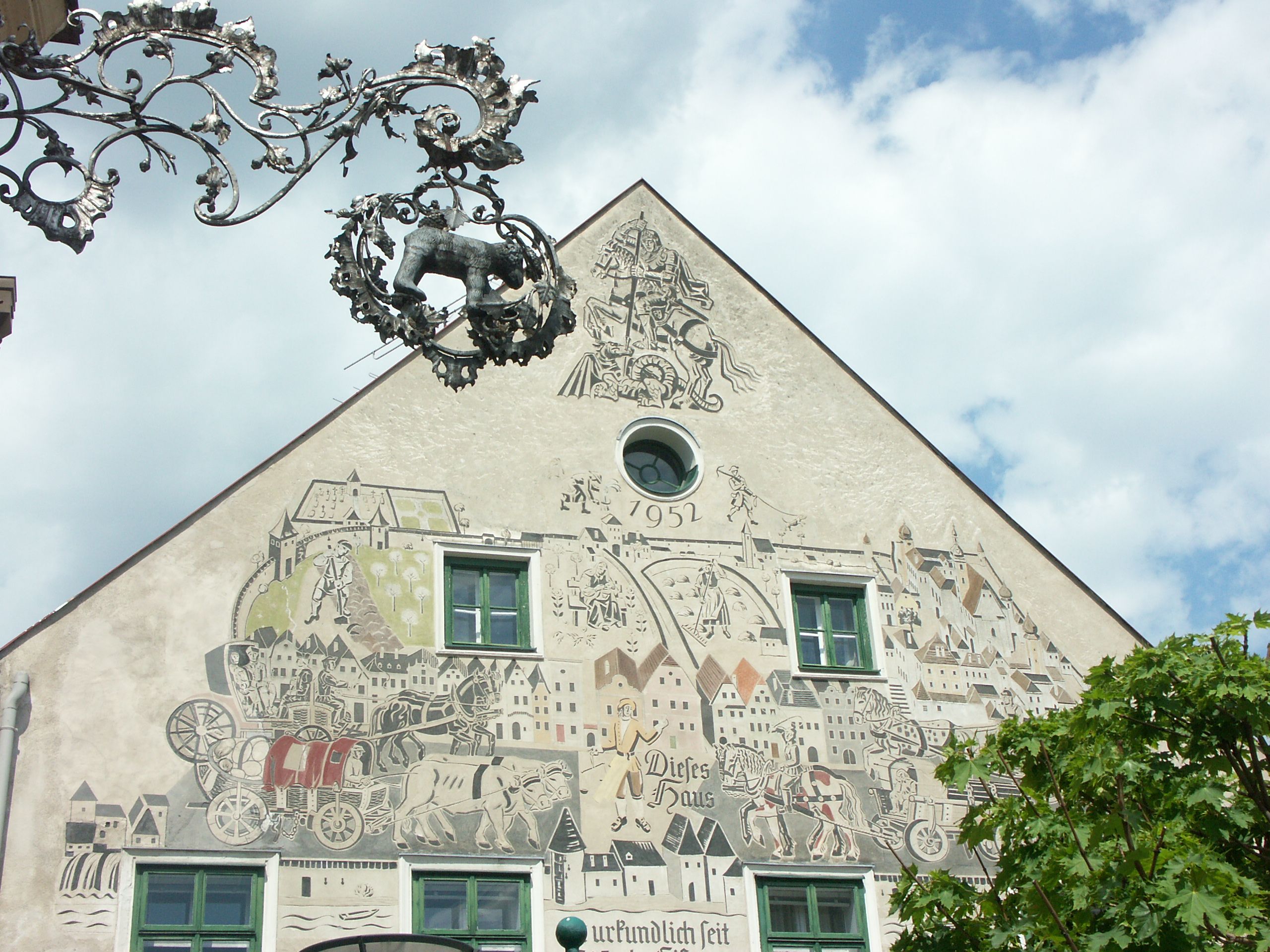 Facade of a house with sgraffito artwork and decorative metal sign.