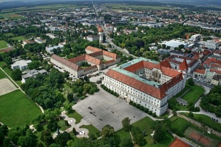 Aerial view of a large, historic complex with red roofs and surrounding green areas.