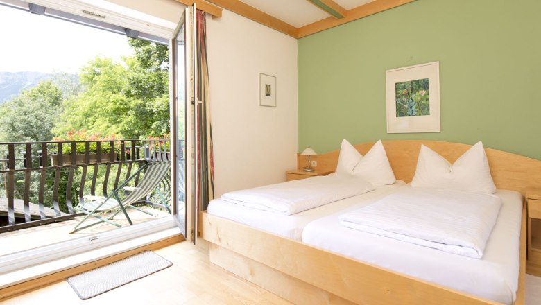 Bright room with double bed, green-painted wall and balcony with mountain view.