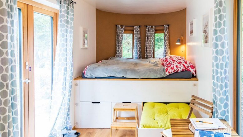 Cozy sleeping area with bunk bed, curtains and small table in a bright room.