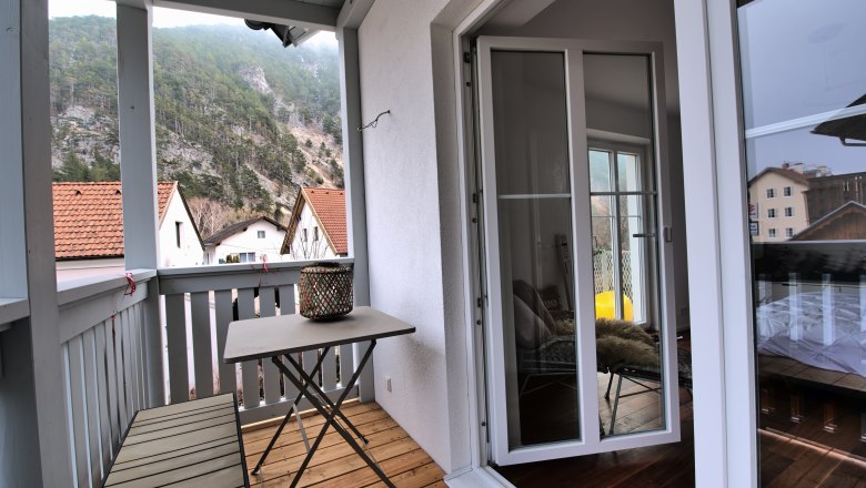 A balcony with a table and bench, surrounded by mountains and houses with red roofs.
