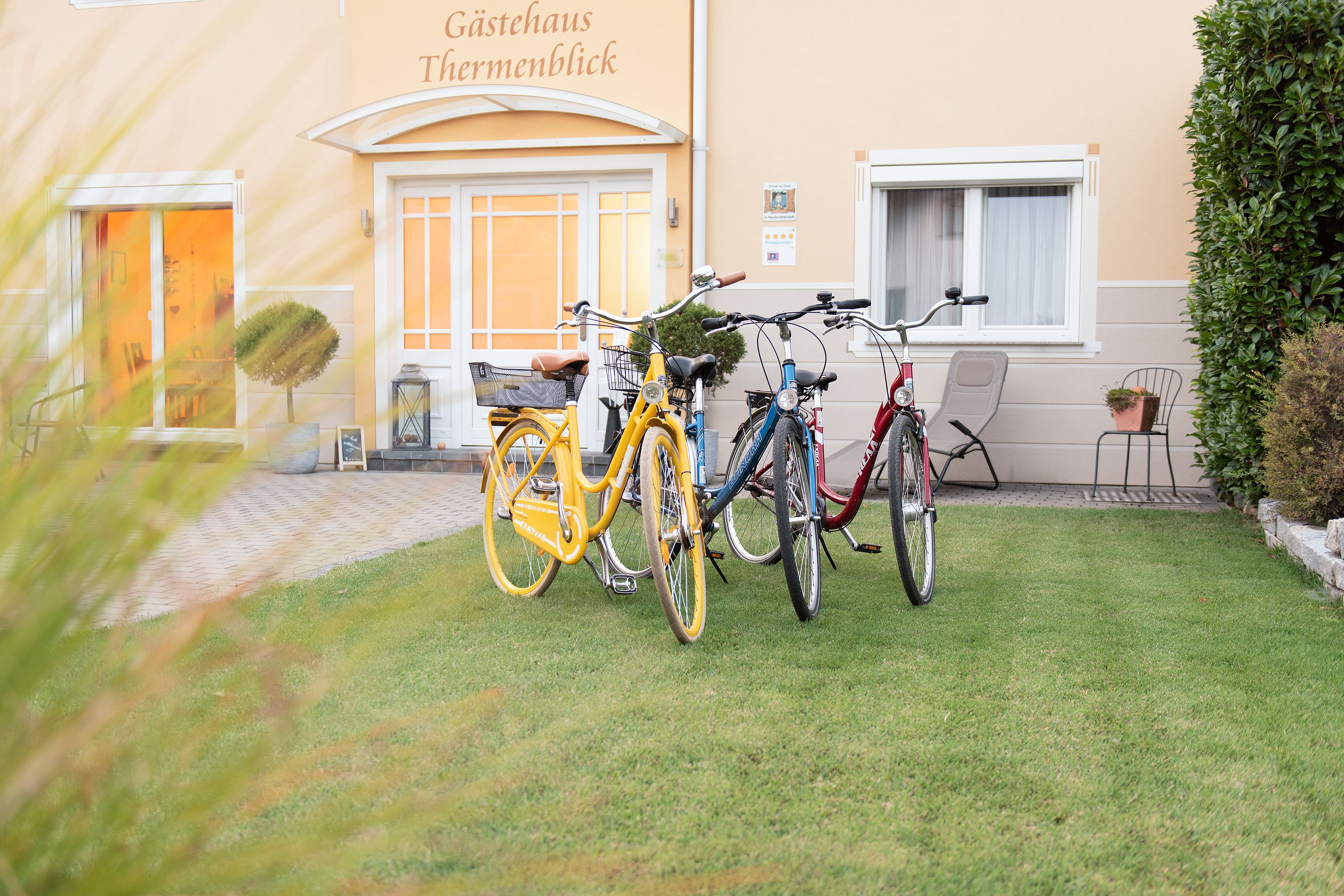 Three bicycles are parked on a lawn in front of the Thermenblick guest house.