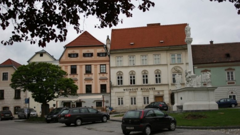 Historic buildings with the sign 'Weingut M&uuml;llner' and a statue on a square.
