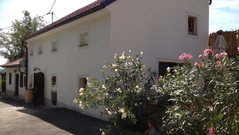 White building with red roof tiles and flowering oleander bushes in front of it.
