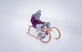 Child in winter clothing sits on a wooden sledge in the snow.