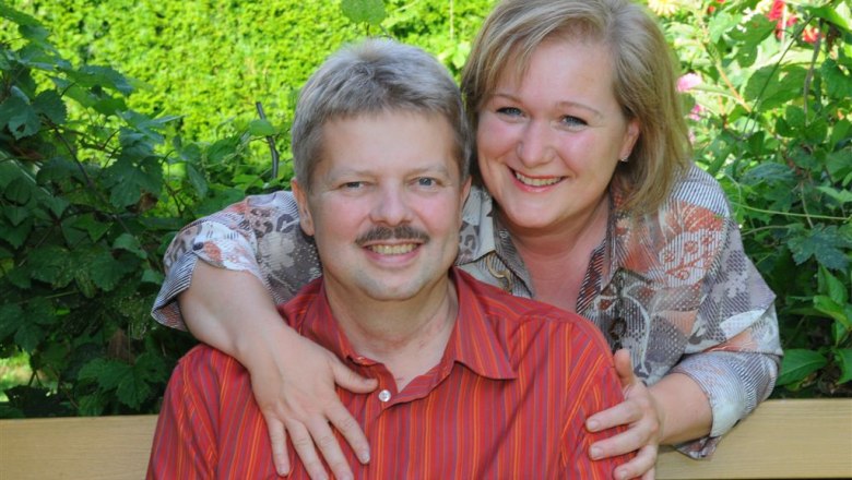 A smiling couple sits on a bench in the garden.