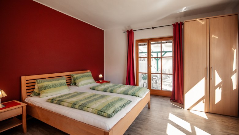 Bedroom with double bed, red wall and wooden furniture.