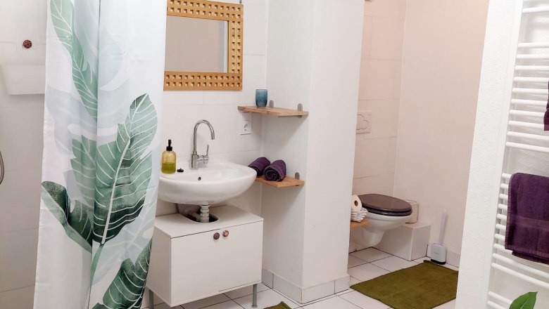 Modern bathroom with white tiles, green carpets and plant motif shower curtain.