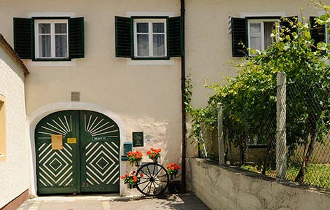 Entrance to a winery with green doors and shutters, decorated with flowers and a wagon wheel.