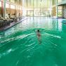 Person swimming in an indoor pool with green water and deckchairs at the edge.
