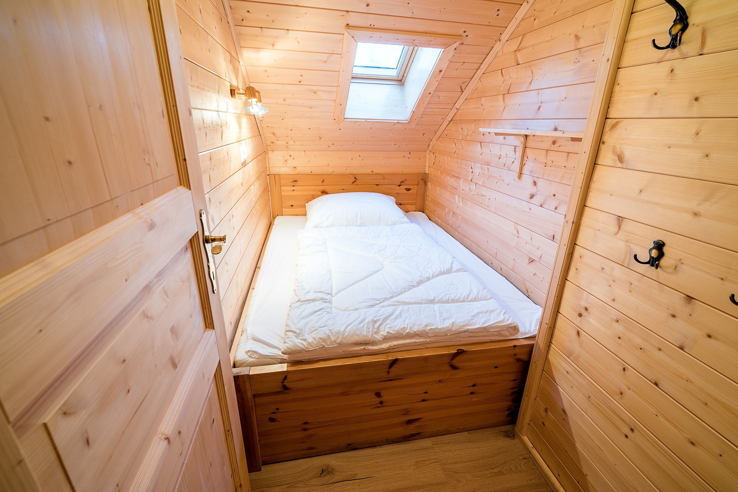 Small children's room with wooden paneling, single bed and skylight.