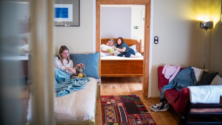 Interior view of a vacation apartment with two rooms. In the foreground a girl is sitting on a bed, in the background two people are reading on another bed.