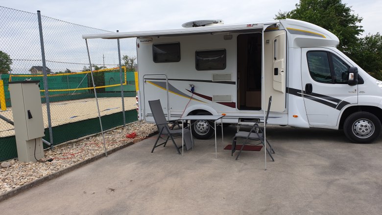 Motorhome with extended awning and camping furniture on a pitch next to a volleyball court.