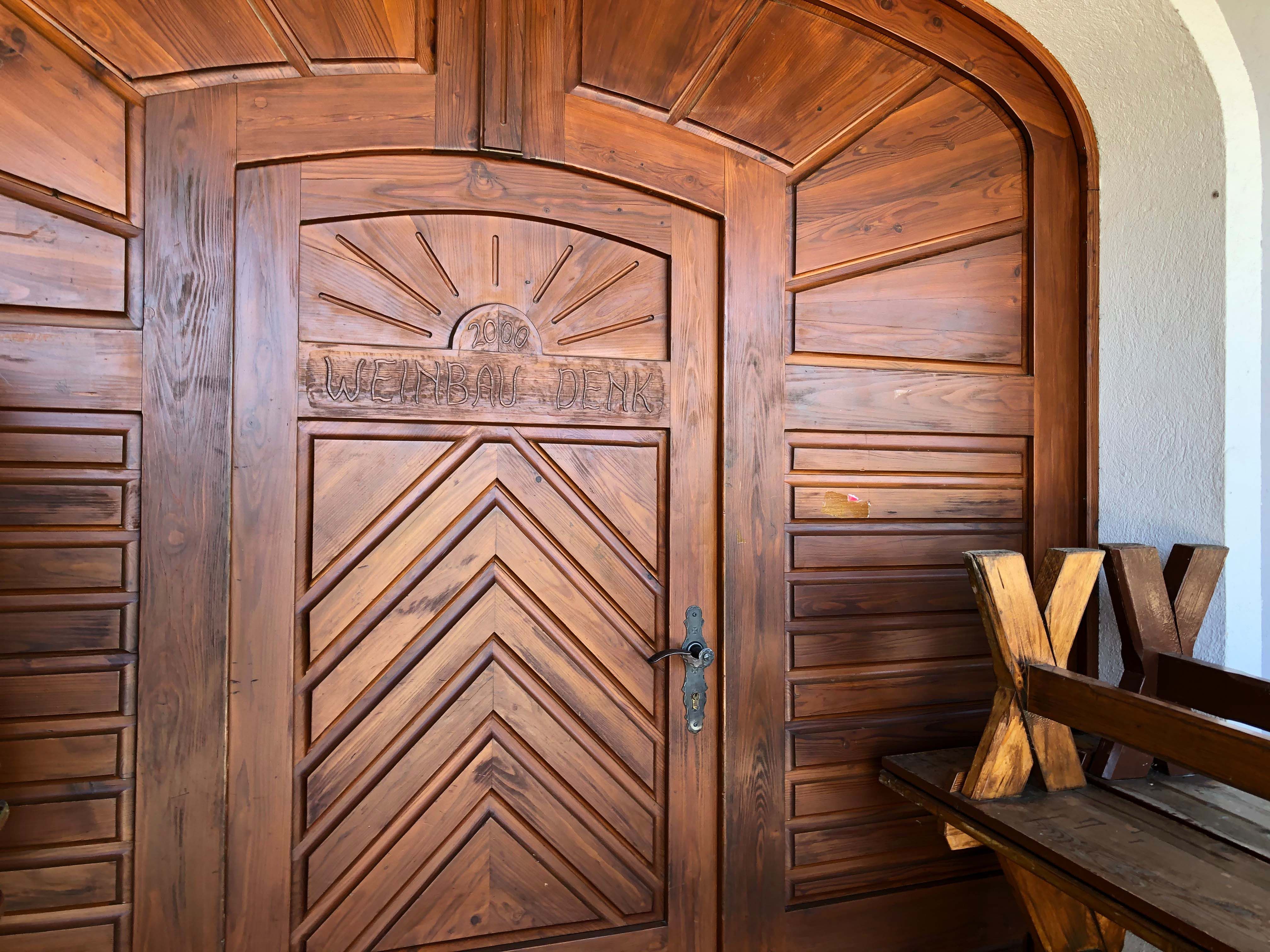 Wooden door with the inscription 'Weinbau Denk' and a sun above it.