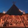 An illuminated tipi tent at night, decorated with fairy lights, prepared for an event.