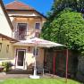 A cozy garden with a parasol, table and chairs in front of a house with a balcony and green climbing plants.