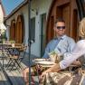 A man and a woman are sitting at an outdoor table in front of a building with wooden doors.