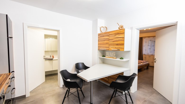 Modern dining area with table, black chairs and wooden cupboards. Decoration with 'HOME' lettering.