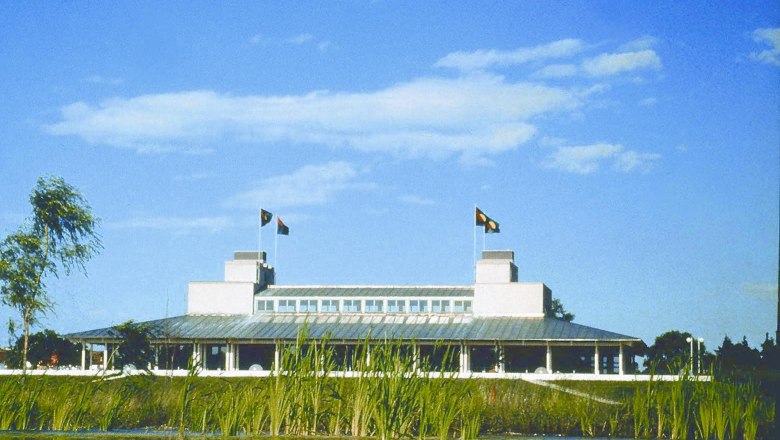 Building of the Golf Club Schloss Ebreichsdorf behind a pond with reeds, blue sky.