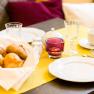 Breakfast table with bread basket, crockery and glasses on a yellow tablecloth.