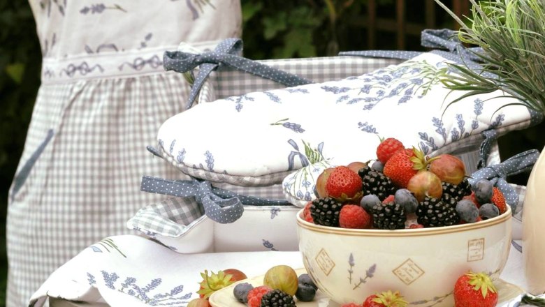 A bowl of berries on a table with lavender decorations and a dressmaker's dummy with an apron in the background.