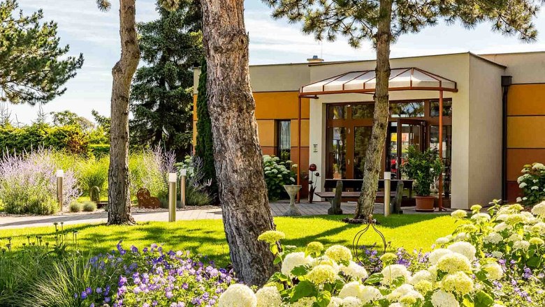 Entrance to a modern building with garden and trees.