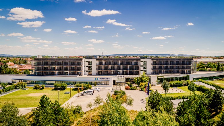Exterior view of the Therme Laa Hotel with green garden and blue sky.