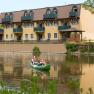 Two people in a canoe on a river in front of a yellow hotel.