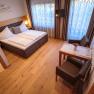 Cozy double room with wooden floor, double bed, small table and chairs, decorative curtains and a TV on the wall.